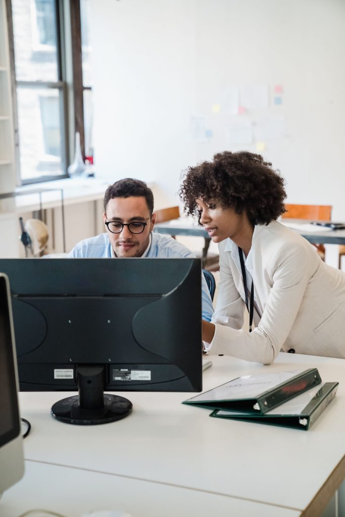 Two professionals collaborate on a computer project in a bright, modern office environment.